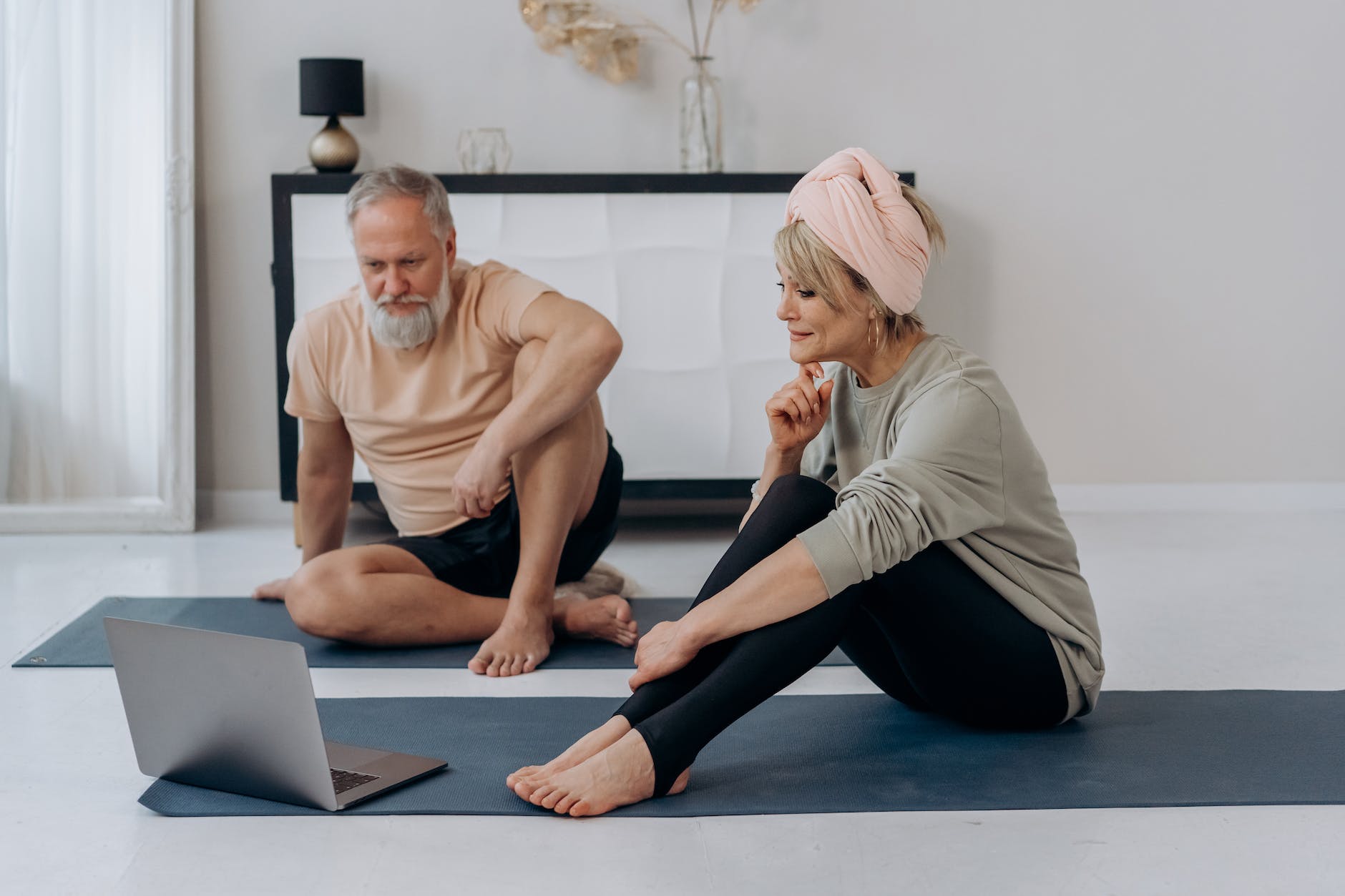 an elderly man and woman sitting on the floor while watching on laptop